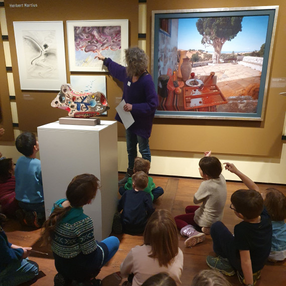 Eine Gruppe von Kindern sitzt auf dem Boden und lauscht einer Führung zu Erlanger Kunst